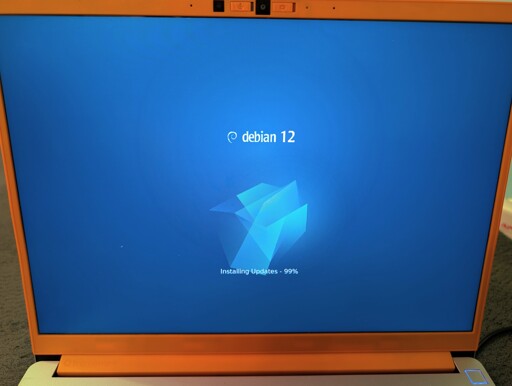 Photo of a laptop running Debian 12, showing software updates on the boot screen.